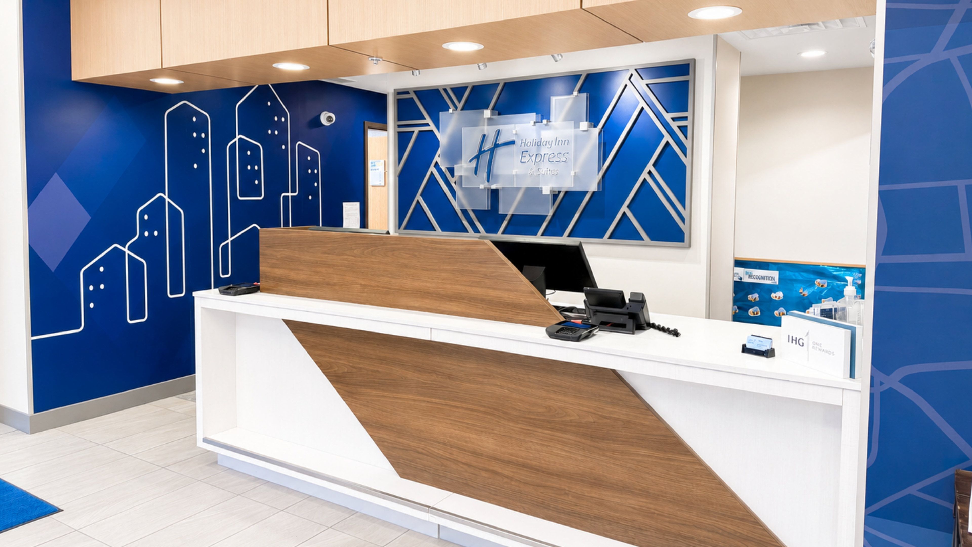A hotel reception desk with a modern design, featuring a wooden accent panel and a digital screen.