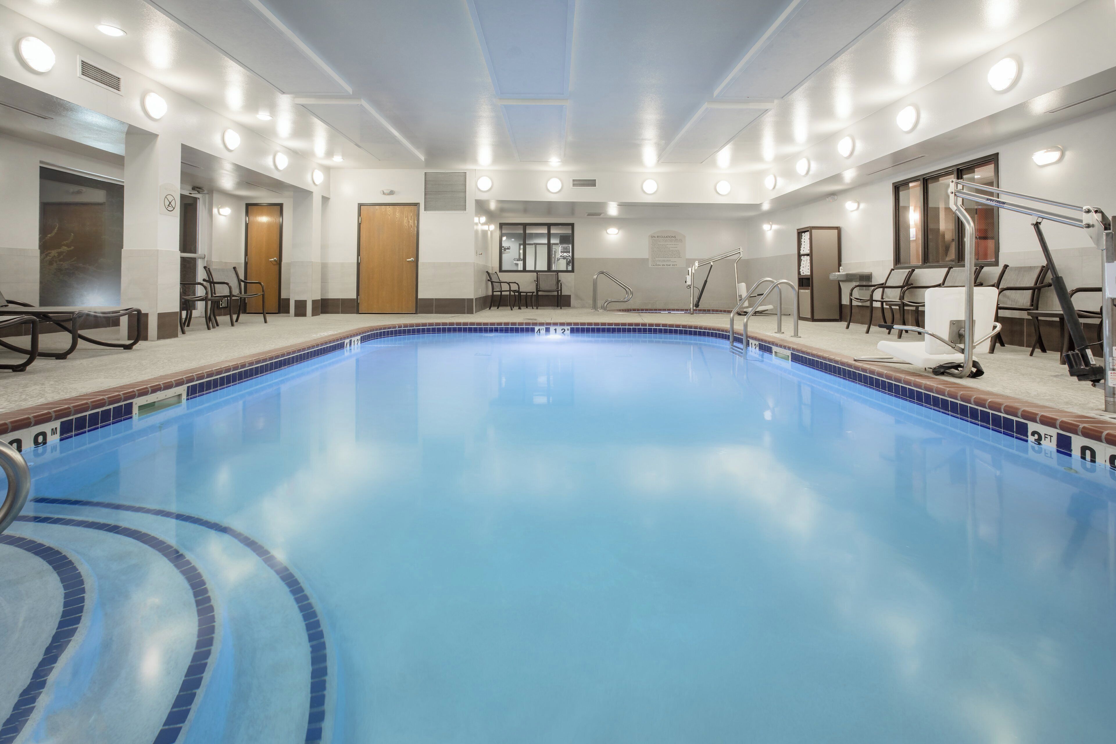 A large indoor swimming pool with clear water, surrounded by lounge chairs and a changing room area.