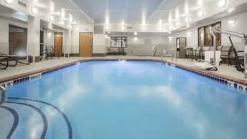 A large indoor swimming pool with clear water, surrounded by lounge chairs and a changing room area.