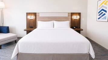A hotel room with a large bed, two bedside tables, a nightstand, a lamp, and a wall-mounted artwork.