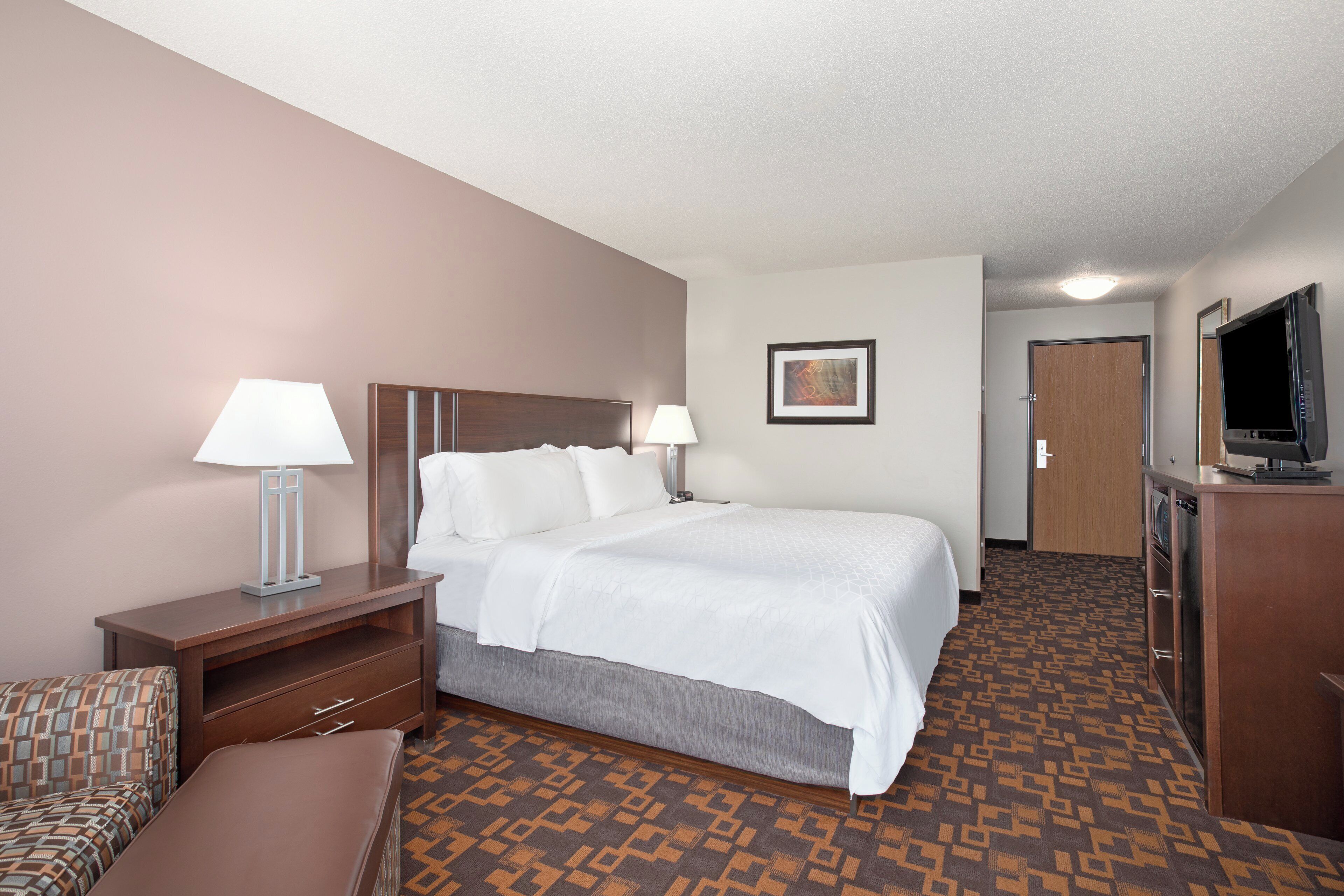 A hotel room with a bed, bedside tables, a TV, a desk, and a patterned carpet.