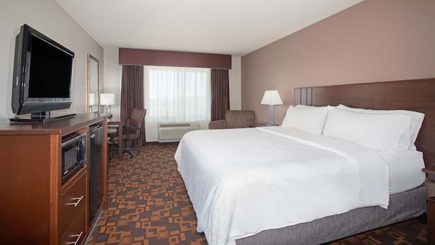 A hotel room with a bed, a desk with a television, a chair, a lamp, and a window with curtains.