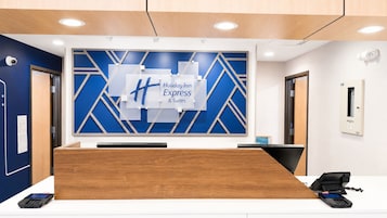 Una recepción con un diseño geométrico azul y blanco en la pared, un letrero de Holiday Inn Express y una cámara de seguridad en la pared.