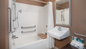 A modern bathroom with a bathtub, shower, and sink. It includes grab bars, a mirror, and a towel rack.