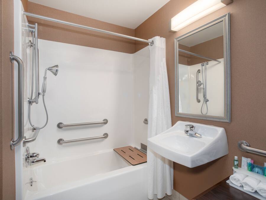 Une salle de bain moderne équipée d’une baignoire, d’une douche et d’un lavabo. Elle comprend également des barres d’appui, un miroir et un porte-serviettes.