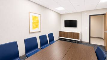 A conference room with a long table, blue chairs, a mounted TV, and a framed picture on the wall.