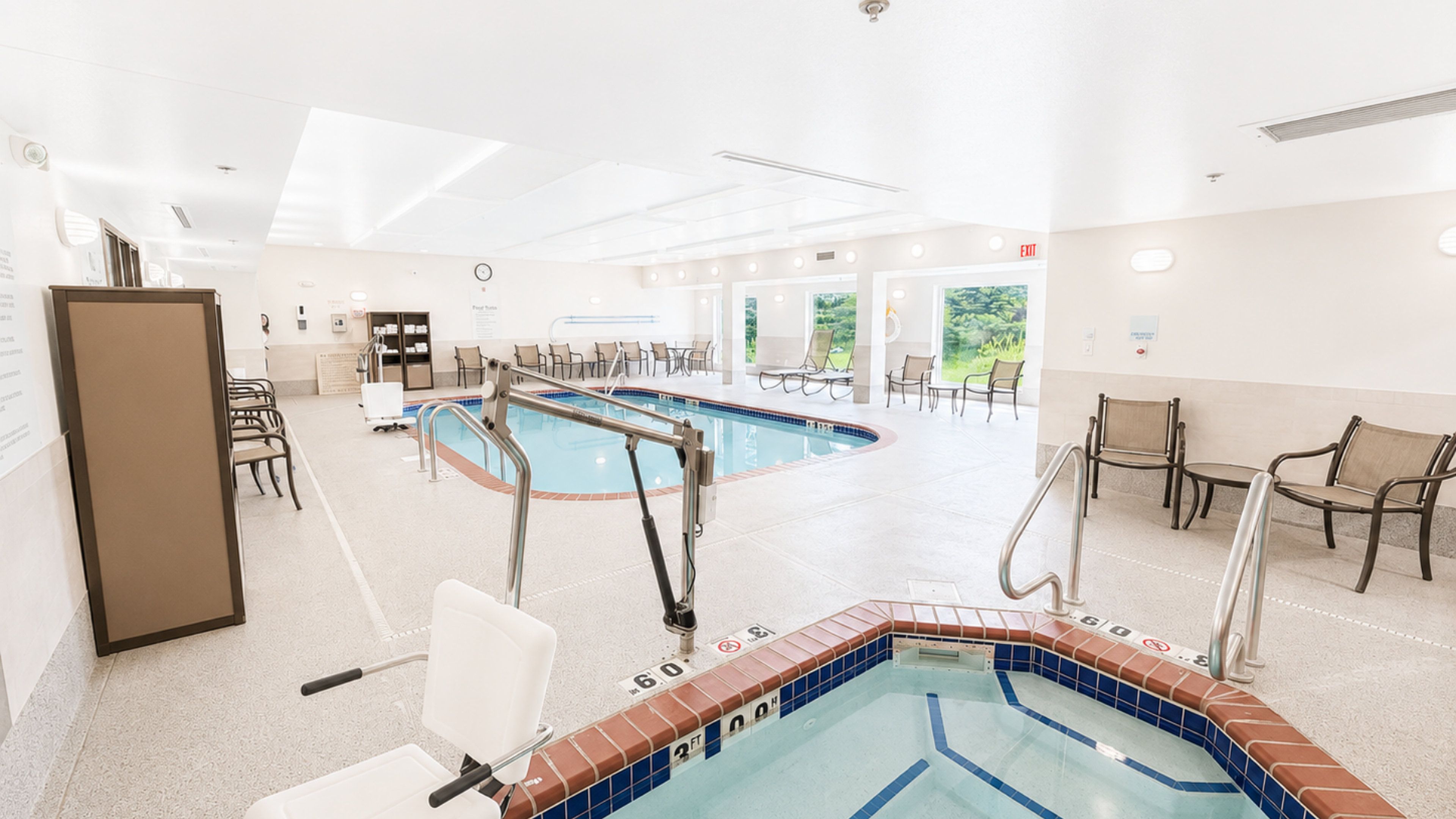 Zona de piscina hotelera con jacuzzi, sillones de descanso y un espacio de estar con vistas al exterior.