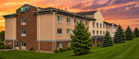 A Holiday Inn Express & Suites hotel with a brick facade, multiple windows, and a lawn with trees.