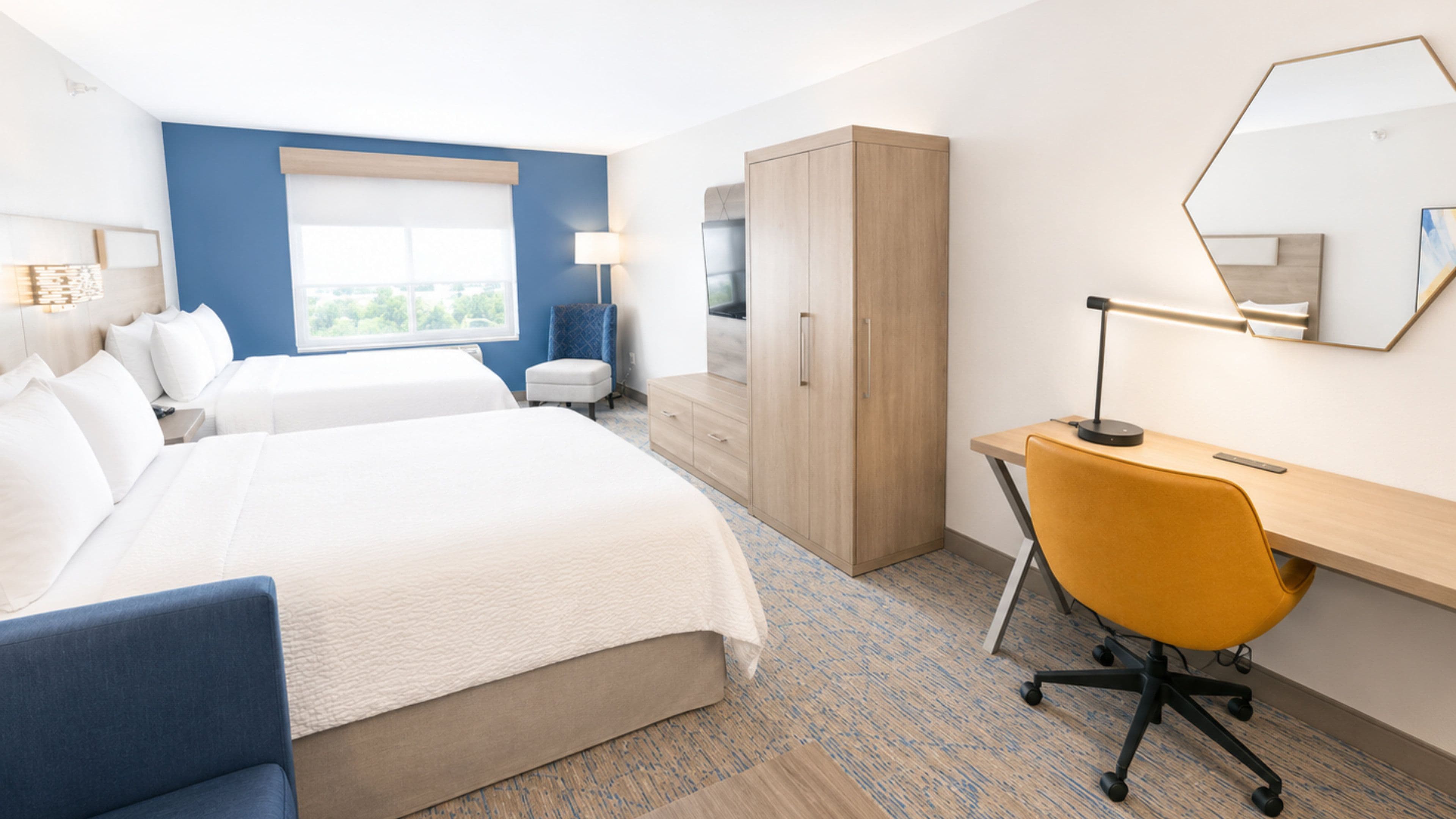 A hotel room with two beds, a desk, a chair, a wardrobe, and a large window.