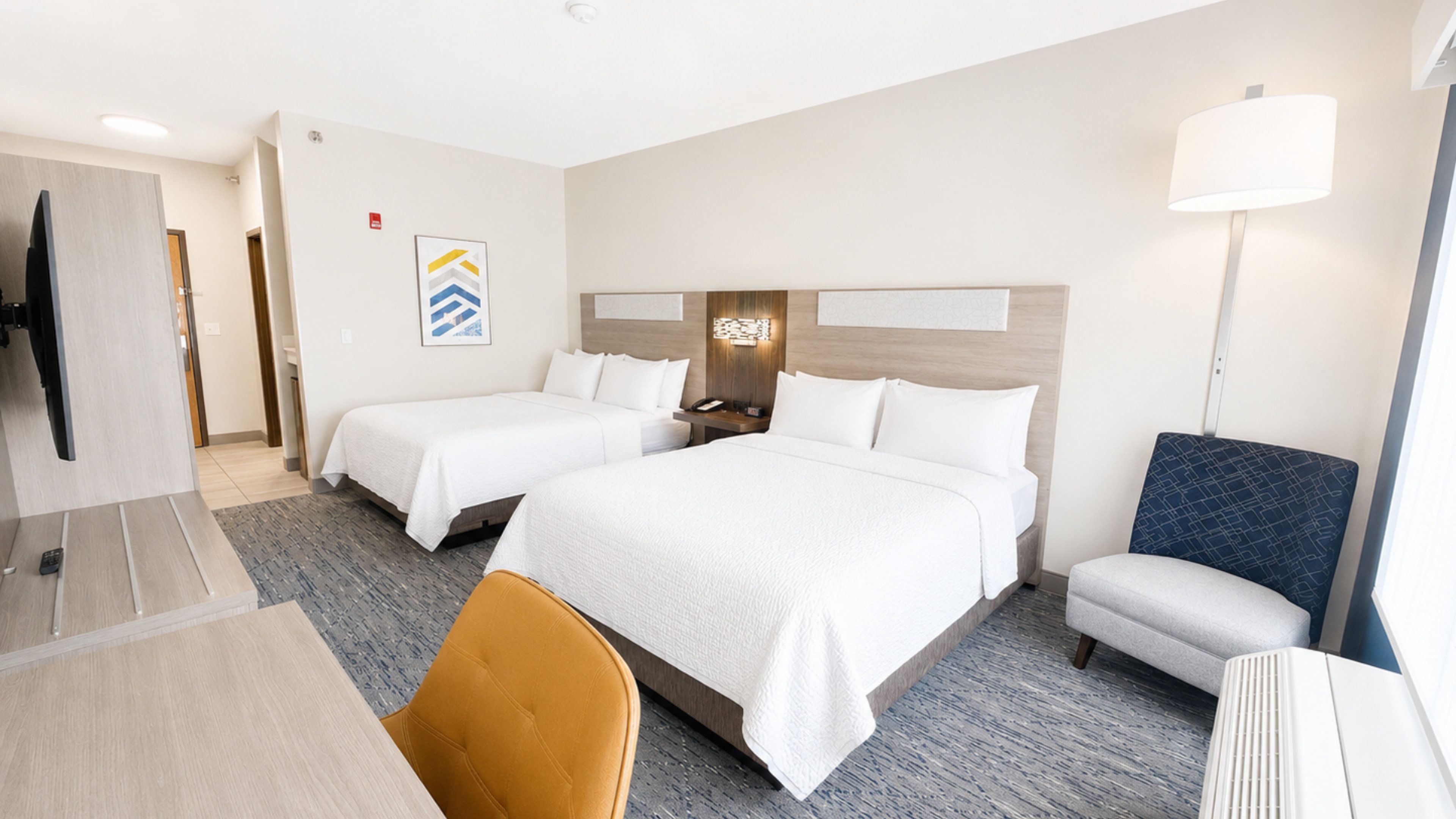 Une chambre d’hôtel avec deux lits, un bureau, une chaise, une télévision et une lampe.