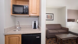 A compact kitchenette with a microwave, coffee maker, and dishwasher. Adjacent is a small seating area with a sofa and a table.