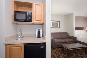 A compact kitchenette with a microwave, coffee maker, and dishwasher. Adjacent is a small seating area with a sofa and a table. - Holiday Inn Express & Suites Yankton by IHG (Yankton)