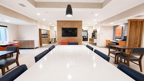 A modern hotel lobby with a large dining table, seating, a flat-screen TV, and a kitchenette area. - Holiday Inn Express & Suites Yankton by IHG (Yankton)