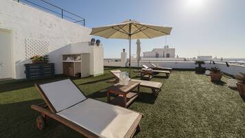 A rooftop terrace with lounge chairs, an umbrella, and potted plants.