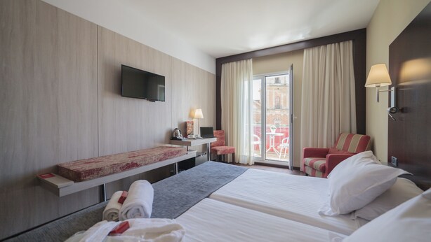 A hotel room with two beds, a TV mounted on the wall, a desk with a lamp, and a view of the outside balcony. - Hotel Salymar (San Fernando)