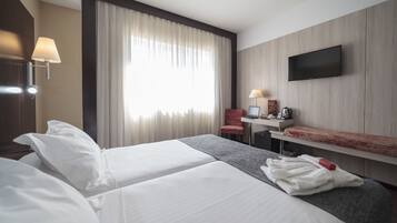 Habitación de hotel con dos camas, un escritorio, una silla, un televisor y una ventana con cortinas.