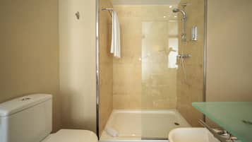 A modern bathroom with a glass-enclosed shower, a white toilet, and a glass sink.