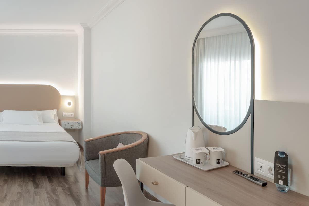 A hotel room with a bed, bedside tables, a chair, a dresser, a mirror, and a coffee maker.