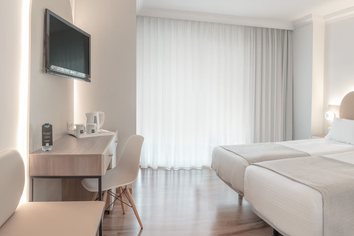 A hotel room with a bed, bedside table, lamp, and a desk with a chair.