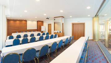 Una sala de conferencias con mesas largas y sillas azules, una pizarra y una puerta de madera.