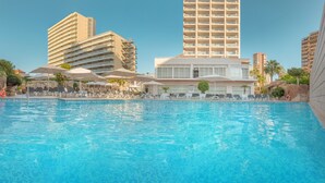 Una piscina con sillas de descanso y sombrillas, rodeada de edificios altos.