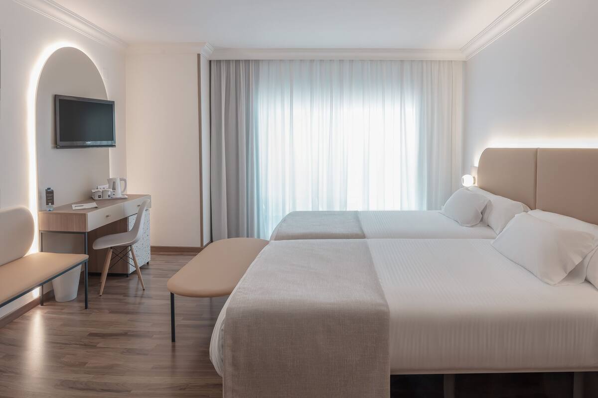 A hotel room with two beds, a desk, a chair, a TV, and a bedside table with a phone.