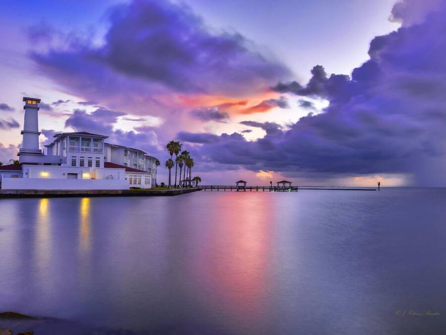 A waterfront property with a lighthouse, a white building, and a pier extending into the water.