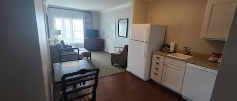 Un espacio habitable compacto con kitchenette, comedor y zona de estar con sofá y televisor.