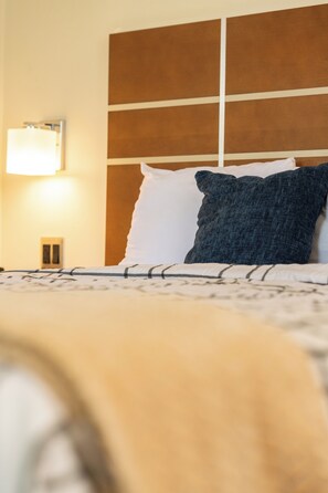 A hotel room with a bed, a nightstand, and a wall-mounted lamp.