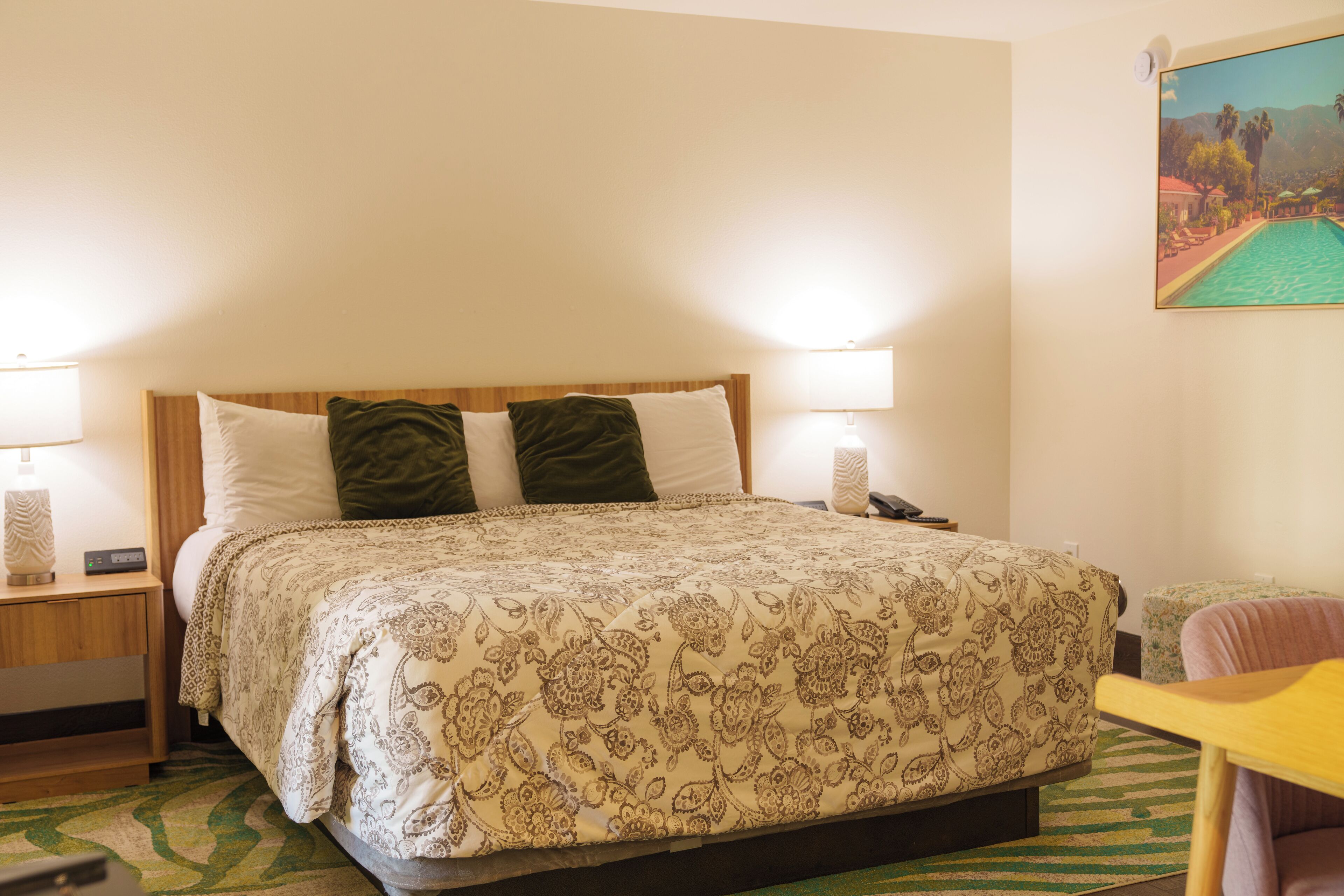 Un dormitorio con cama, dos lámparas de noche, una mesita de noche, una silla y un cuadro en la pared.