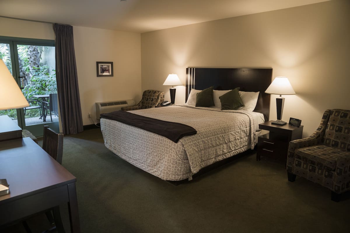 A hotel room with a large bed, two bedside tables with lamps, a chair, and a desk.