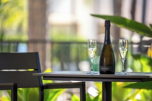 A table with a bottle of wine and two glasses on it, set outdoors with greenery in the background.