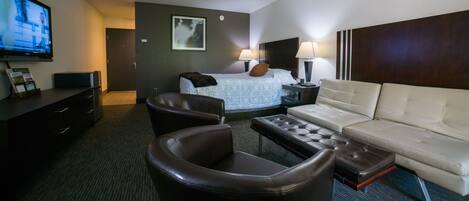A hotel room with a bed, a sofa, a chair, a TV, and a desk.