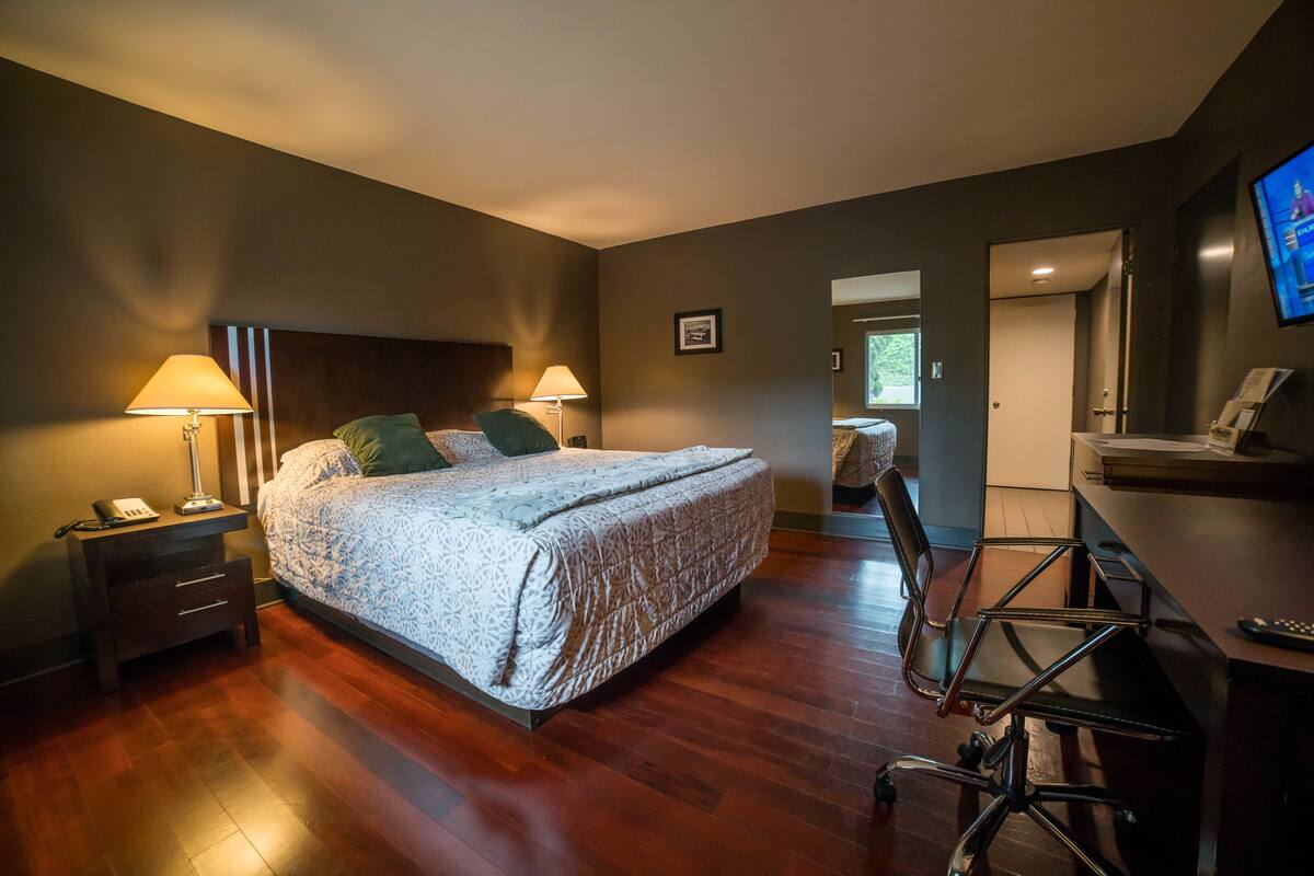 A bedroom with a bed, bedside lamps, a desk with a chair, and a TV on the wall.