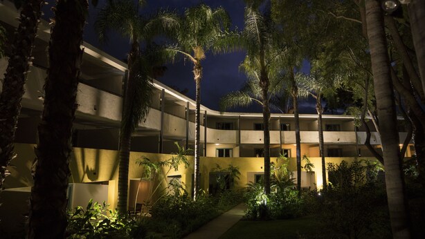 A multi-story hotel with a courtyard surrounded by palm trees and greenery, featuring a well-lit entrance and multiple balconies. - Lemon Tree Inn (Santa Barbara)