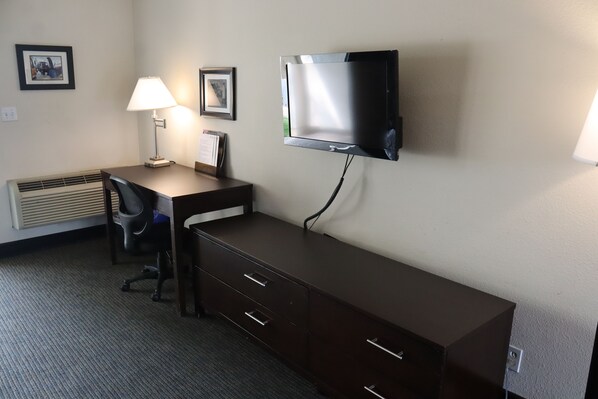 A hotel room with a desk, chair, TV, and a lamp.