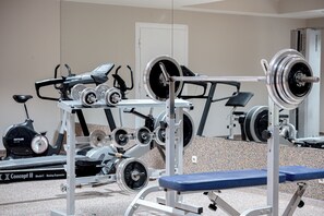Ein Fitnessraum mit Trainingsgeräten, einer Bank und einer Tür im Hintergrund.