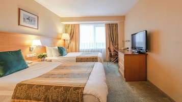 A hotel room with two beds, a desk with a television, a chair, and a window with curtains.