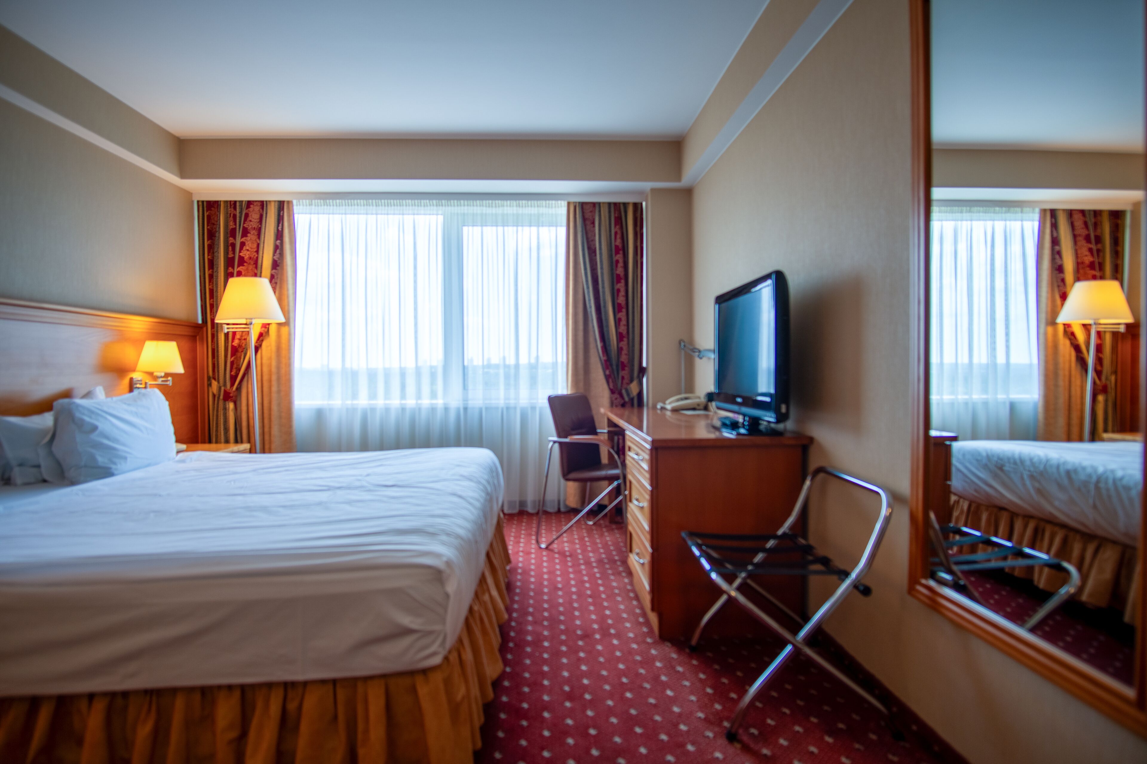 A hotel room with a large bed, a desk with a chair, a television, and a mirror.