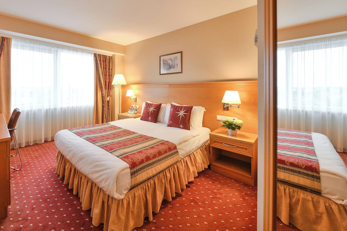Une chambre d’hôtel avec un grand lit, deux tables de chevet avec des lampes, un petit bureau et un miroir.