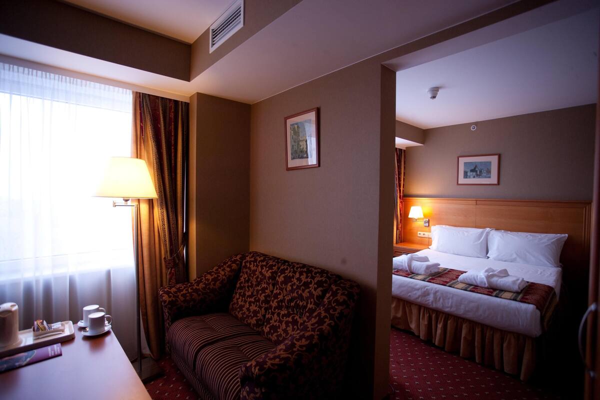 Une chambre d’hôtel avec un lit, un canapé, un bureau avec une lampe et une fenêtre avec des rideaux.