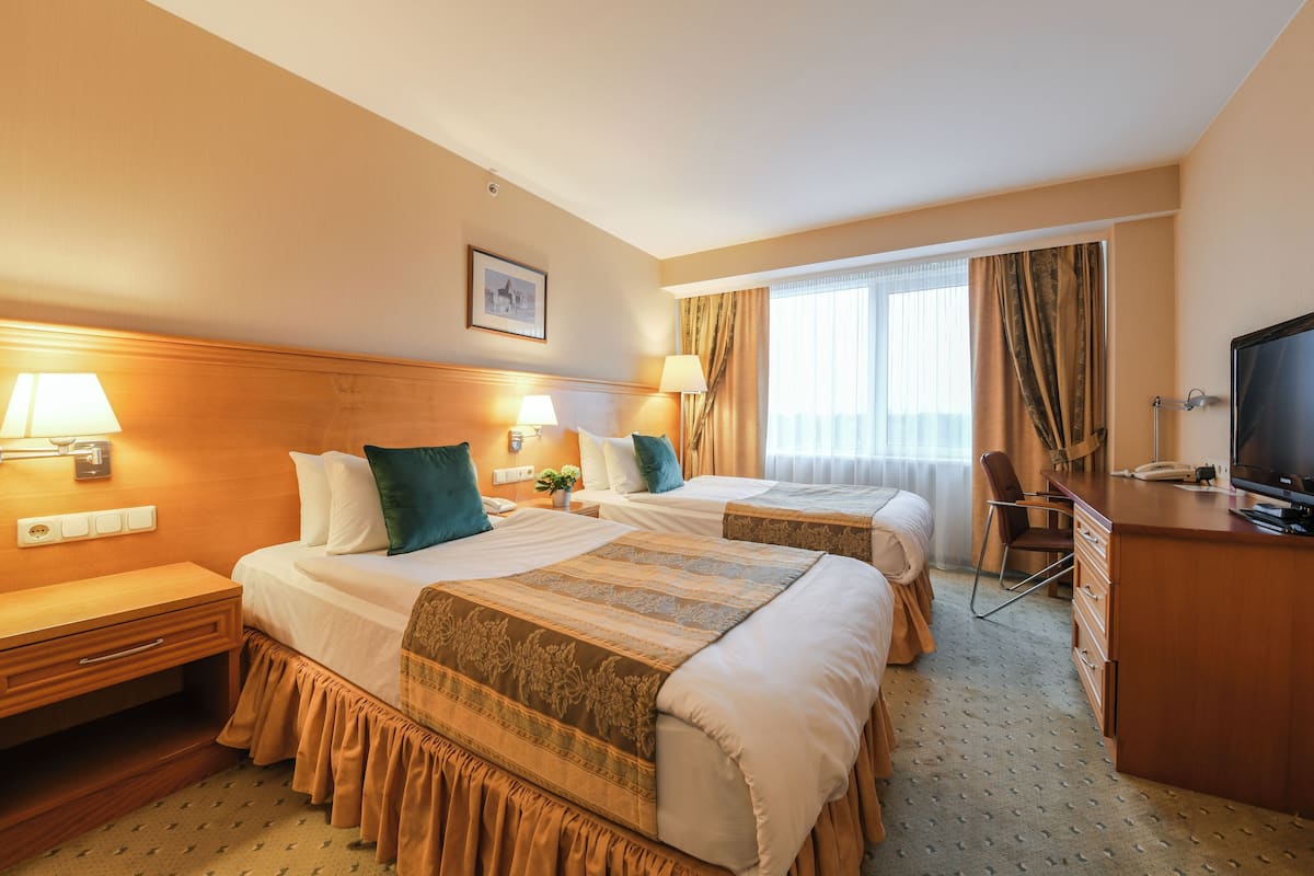 Une chambre d’hôtel avec deux lits, un bureau, une télévision et une fenêtre avec des rideaux.