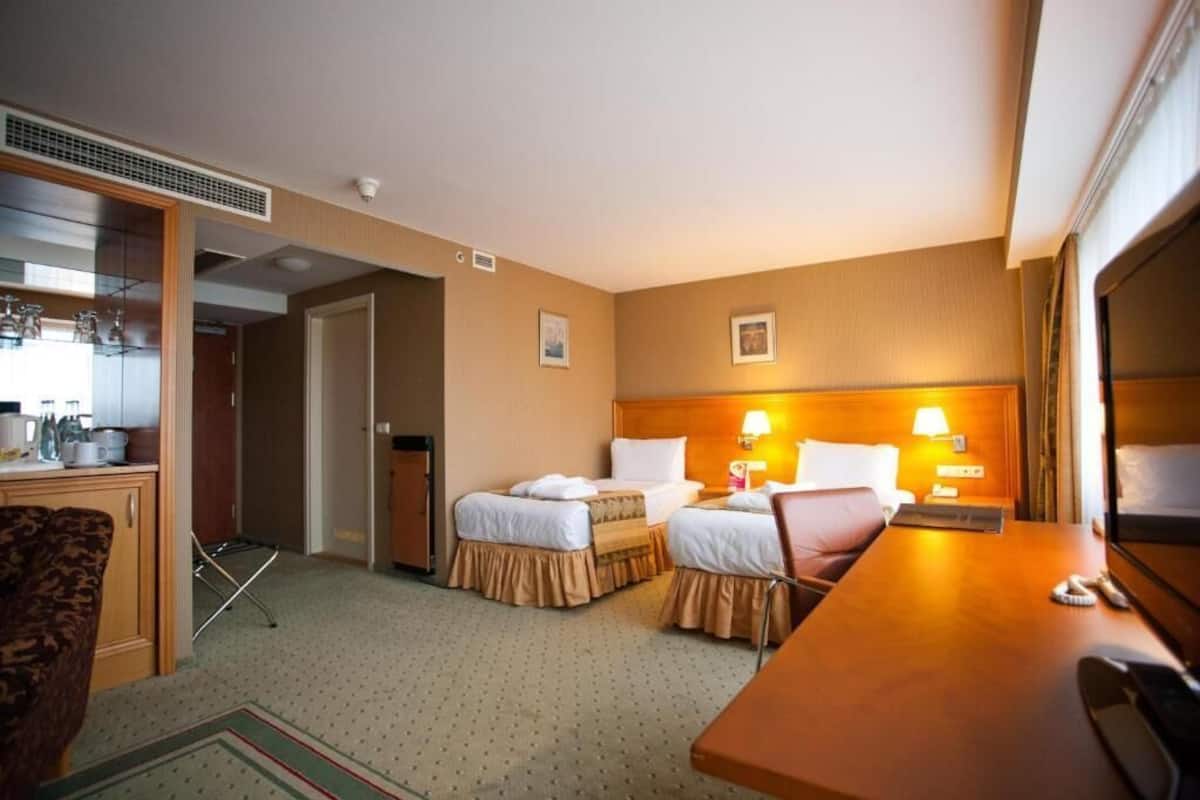 Une chambre d’hôtel avec deux lits, un bureau, une chaise, une petite kitchenette et une salle de bain.