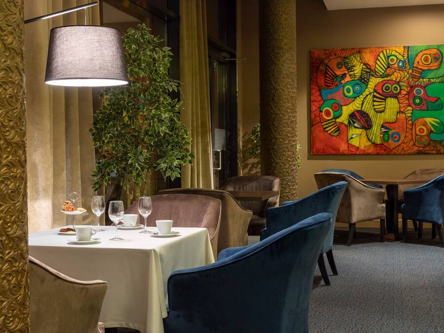 A dining area with a table set for two, a lamp, and a colorful abstract painting on the wall.