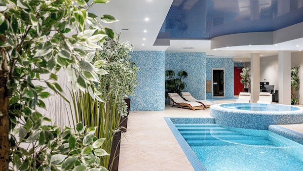 A modern indoor pool area with lounge chairs, a hot tub, and indoor plants.