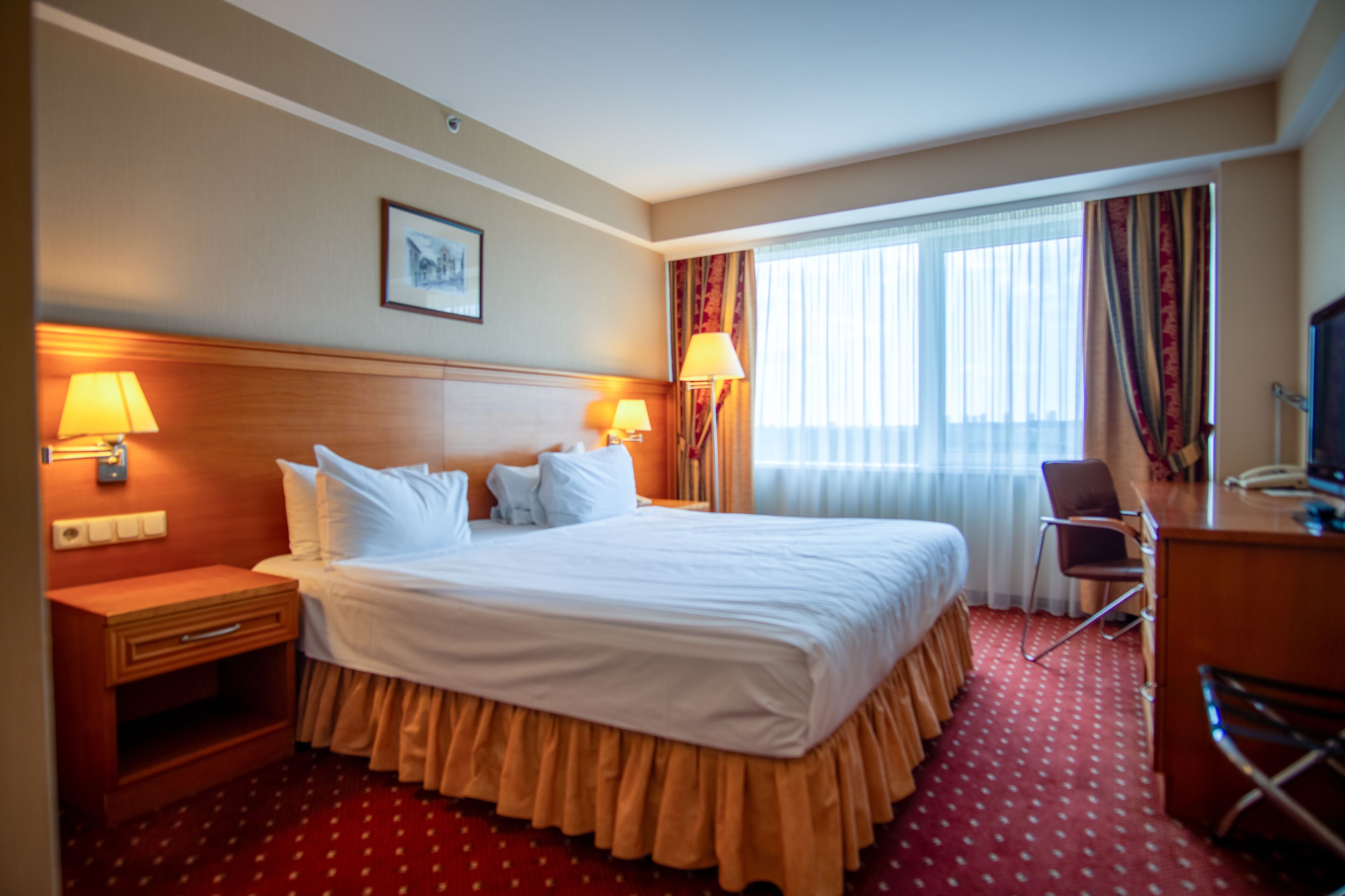 Habitación de hotel con una cama grande, dos lámparas de noche, un escritorio con una silla y un televisor.