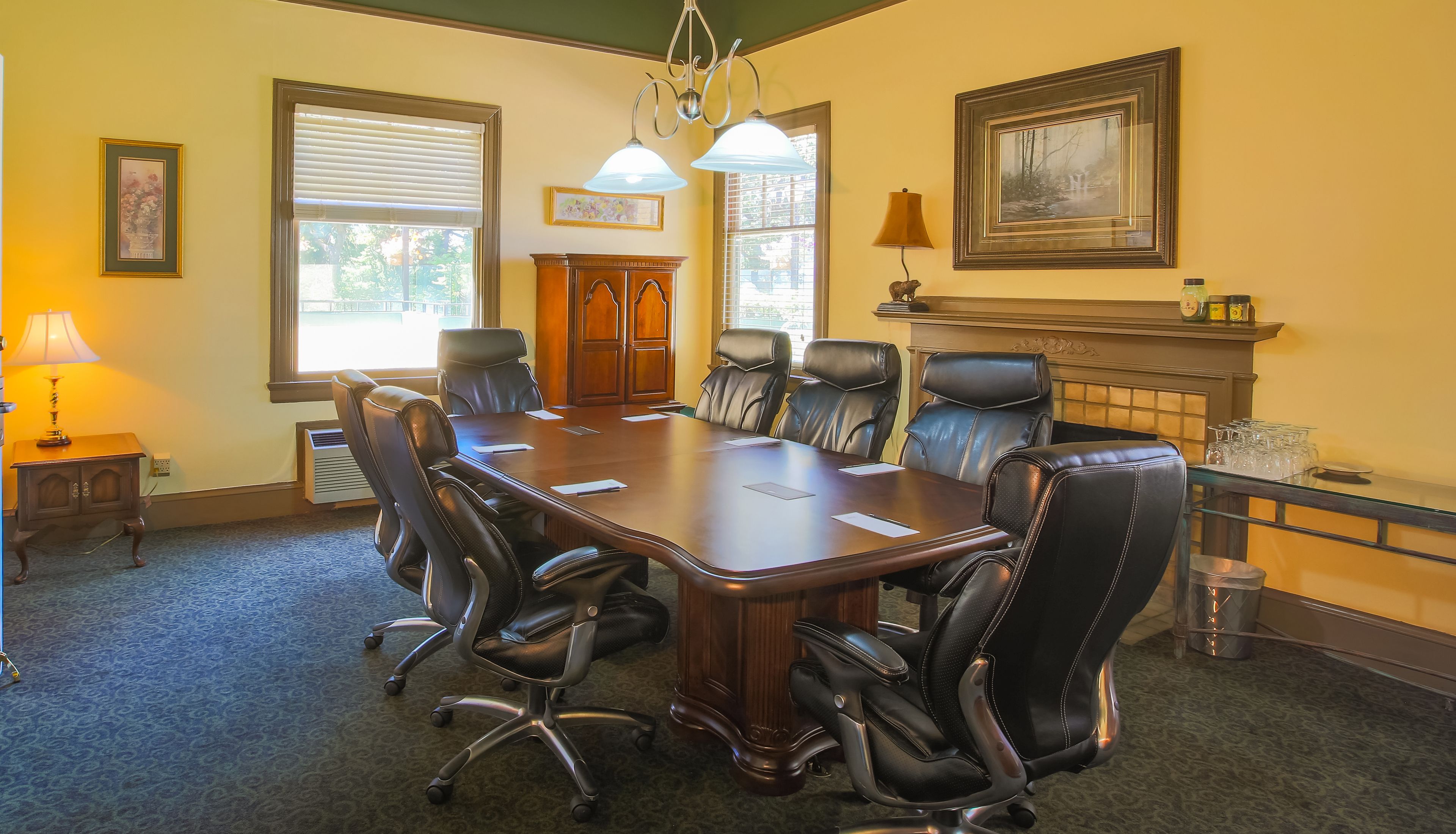Une salle de conférence dotée d’une grande table en bois, de fauteuils en cuir, d’une cheminée et d’œuvres d’art encadrées qui ornent les murs.