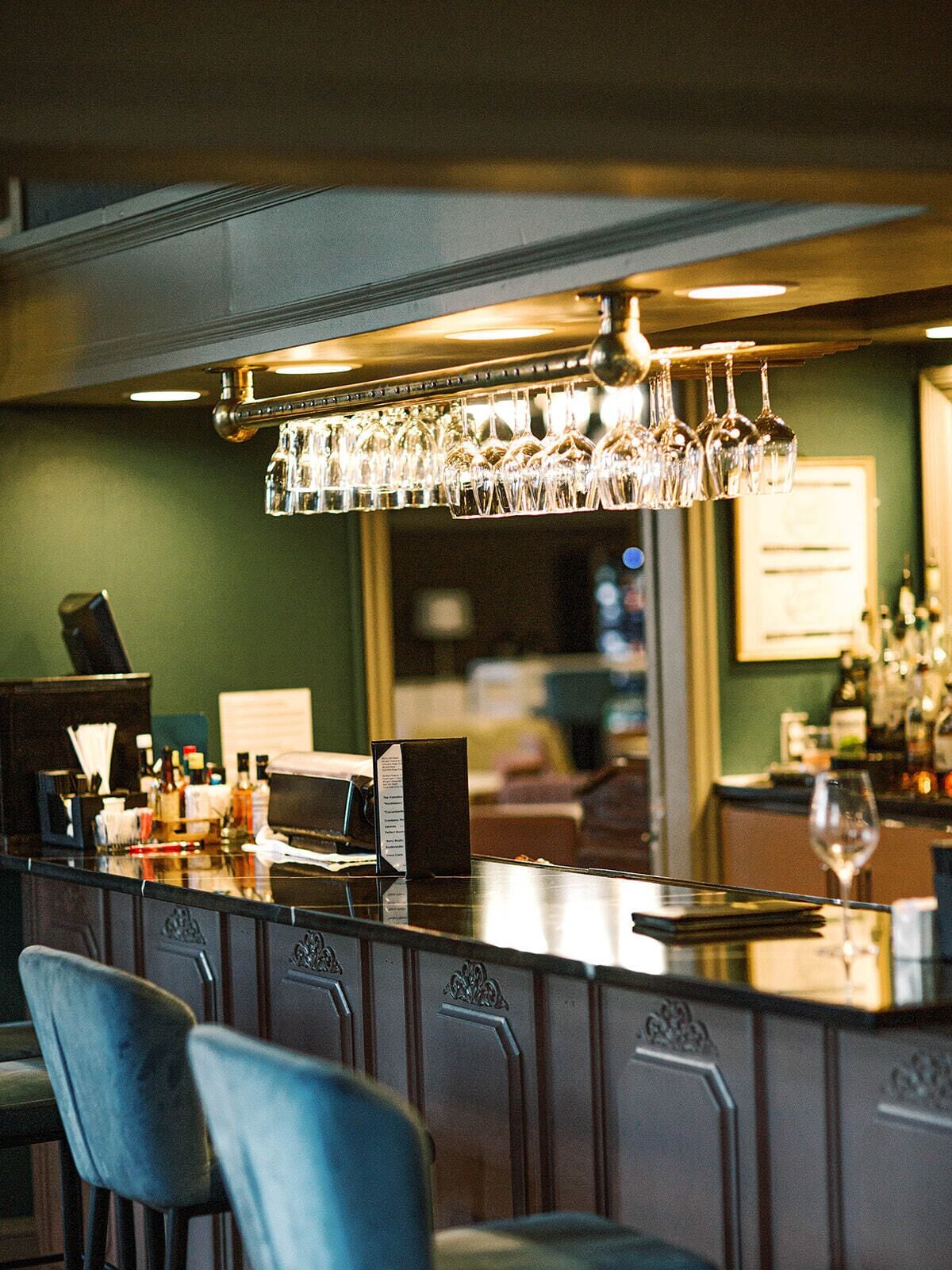 A bar area with a counter, hanging wine glasses, and bar stools.