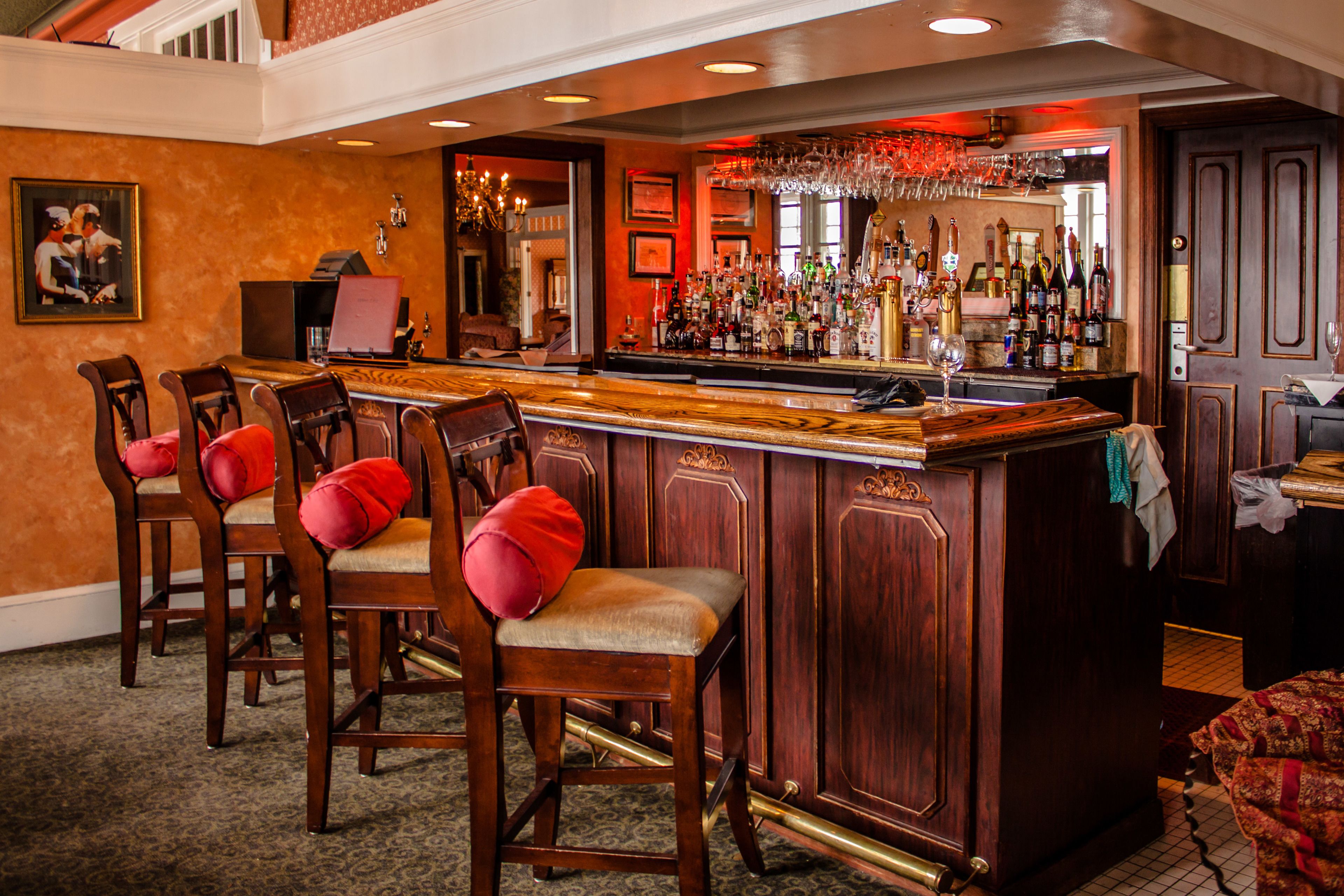 A bar area with wooden bar stools, a bar counter, and a variety of bottles and glasses.