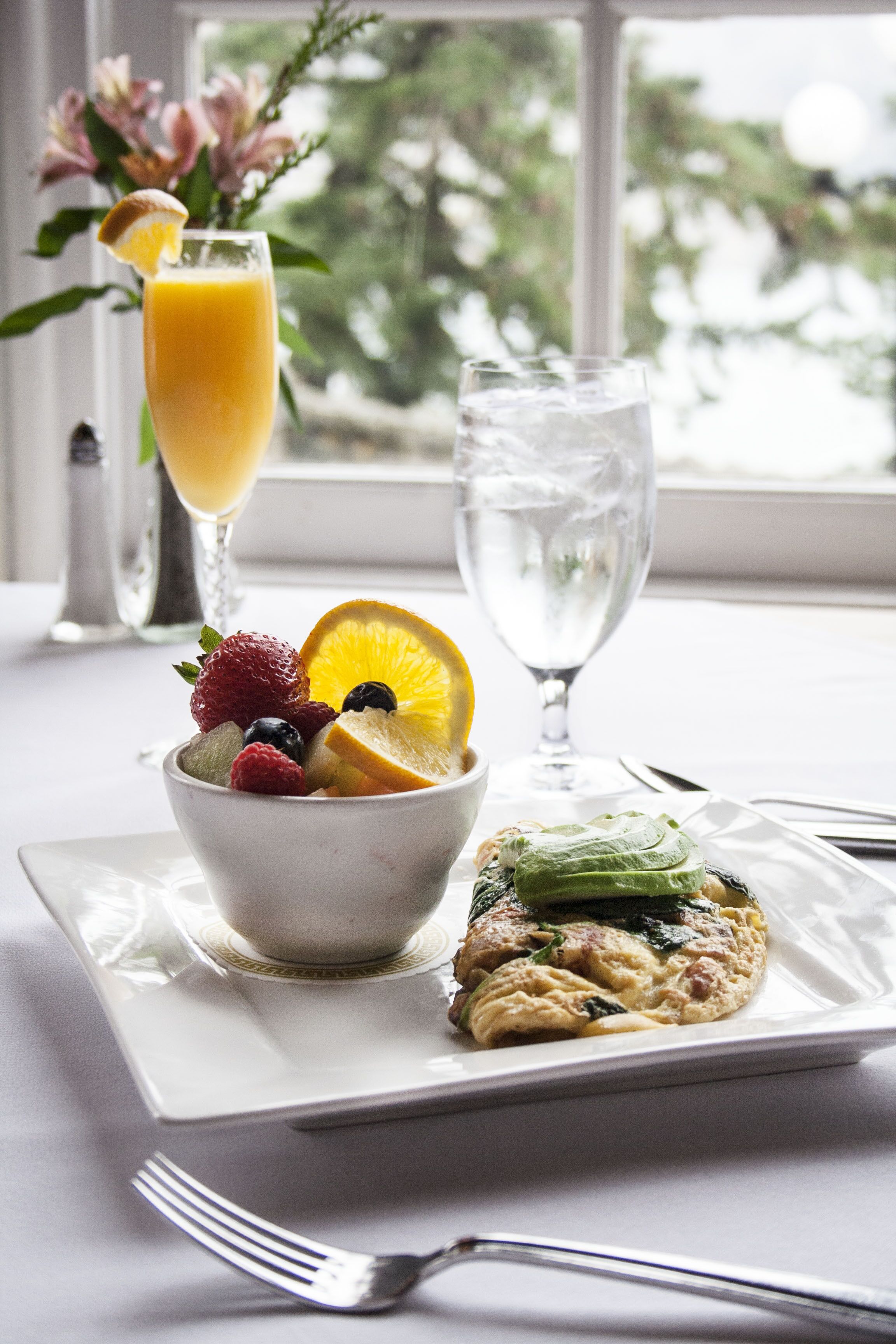 A breakfast setting with a bowl of fruit, a glass of orange juice, a glass of water, and a plate with a pastry.